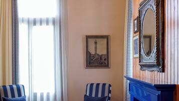 Una habitación con una mesa redonda, dos sillas a rayas, un florero con flores, una chimenea y un cuadro en la pared.