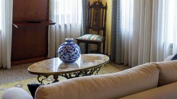 A living room with a chandelier, a television, a sofa, a table with a vase, and curtains.