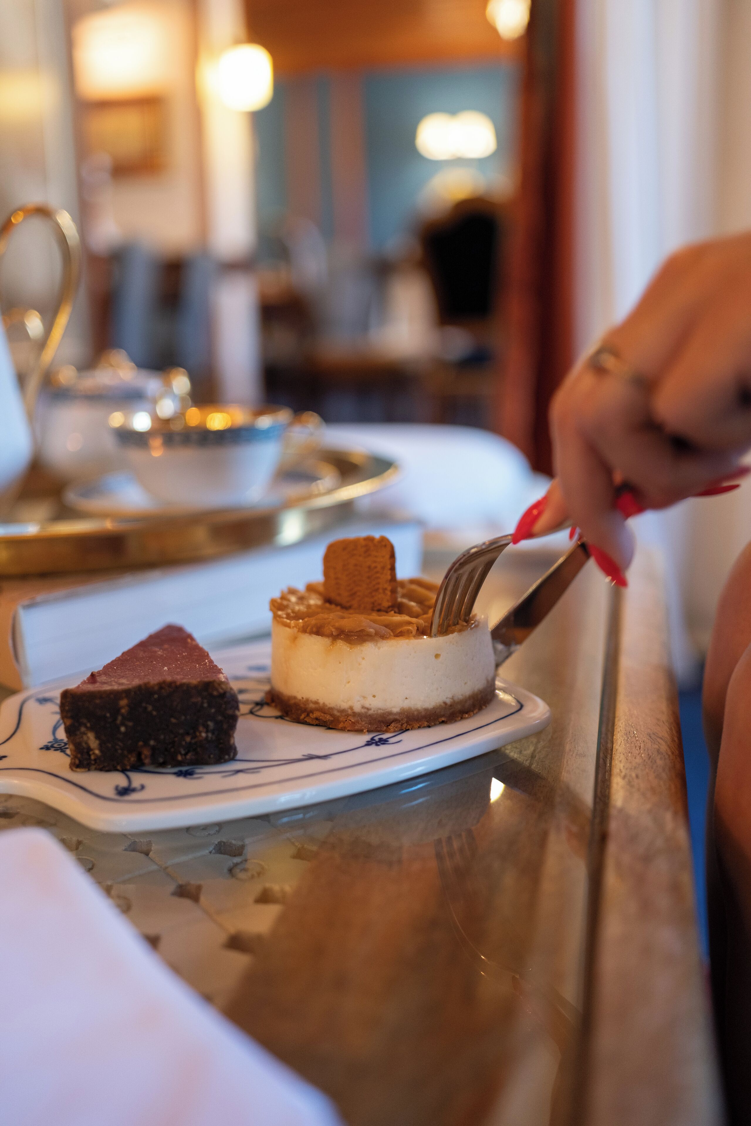 Een desserttafel met verschillende taarten en iemand die een cheesecake aansnijdt.