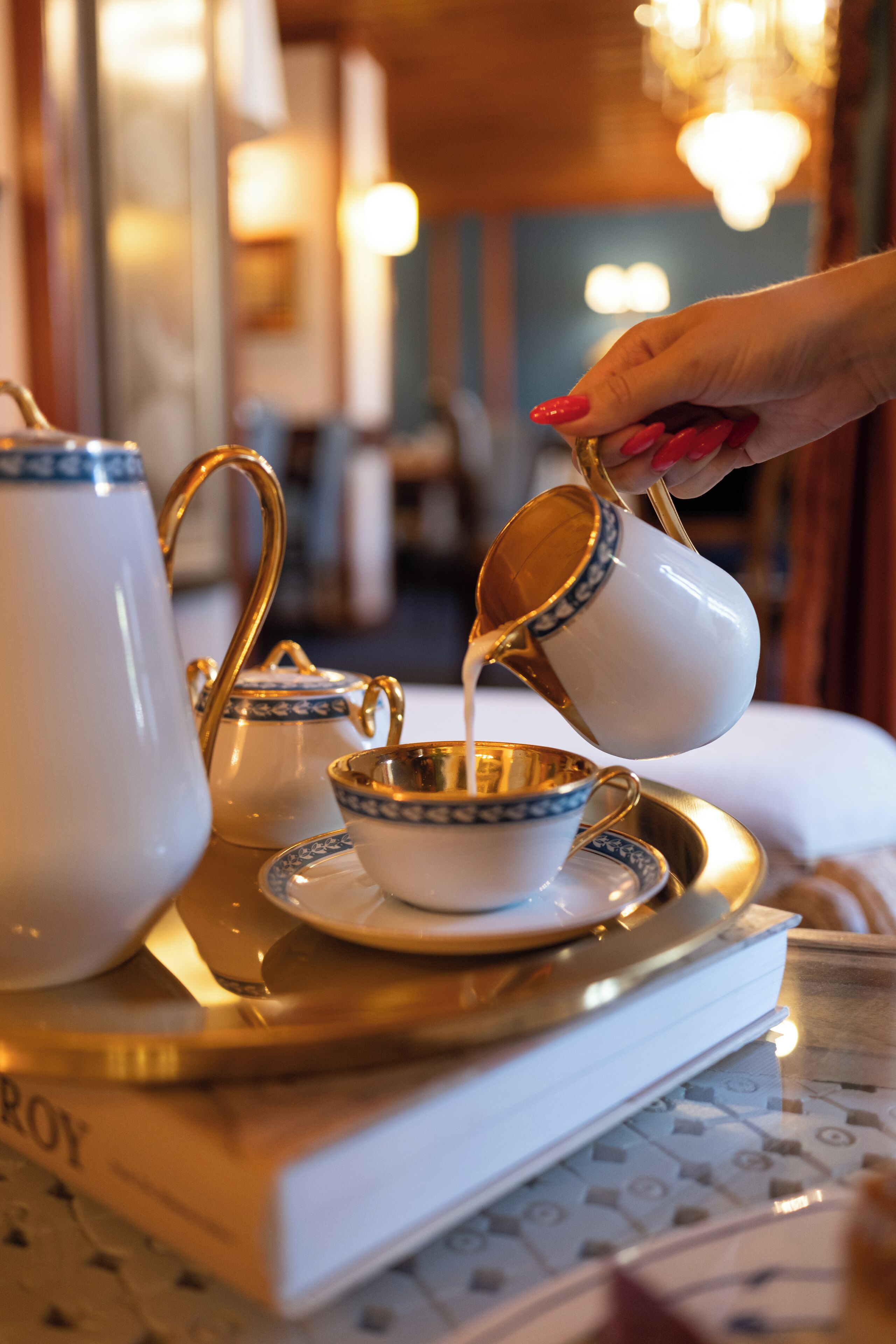 A tray with a teapot, cups, and saucer, with a hand pouring liquid into a cup.