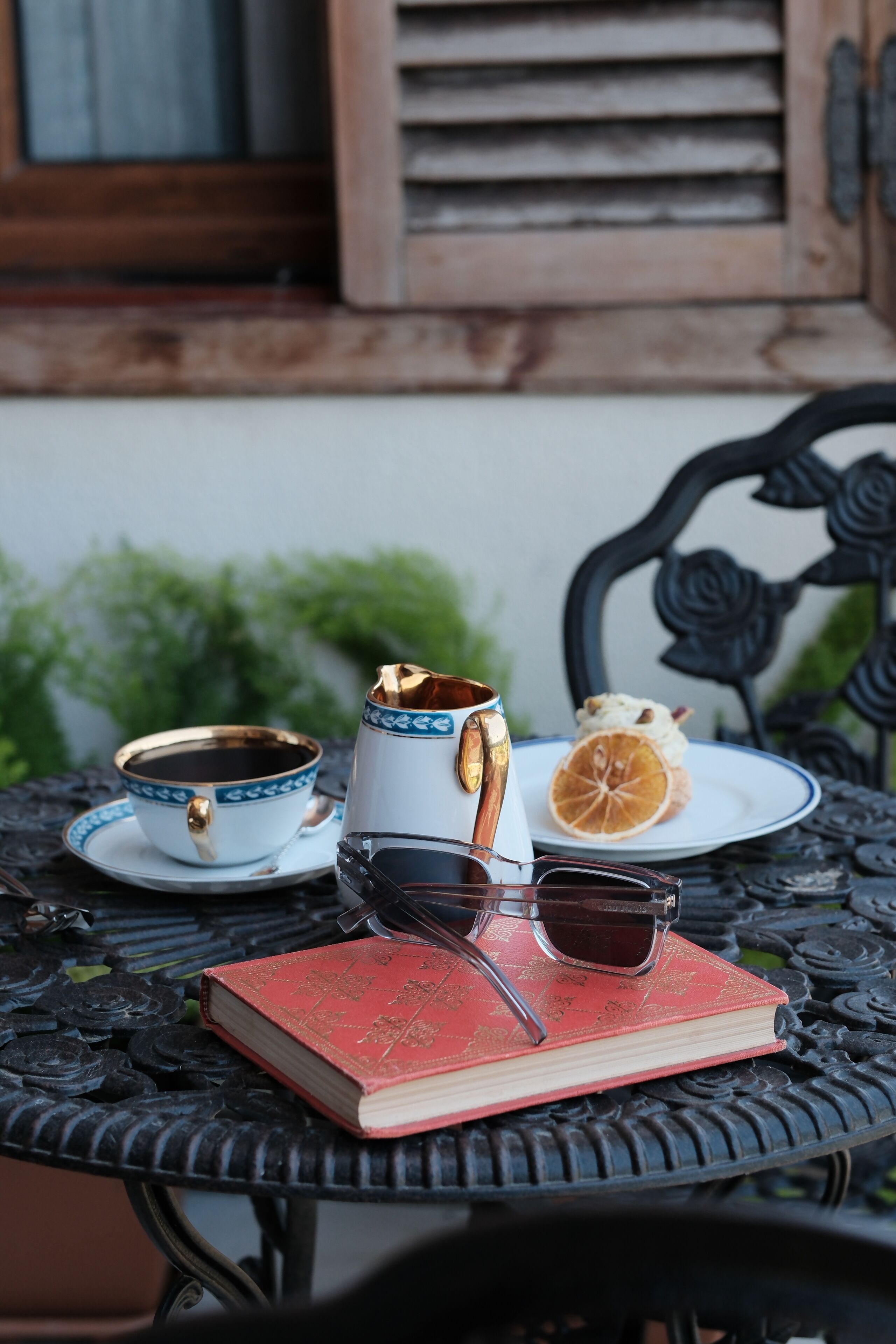 A table with a book, a cup, a saucer, a teapot, and a slice of orange.
