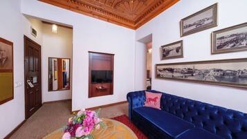 A room with a blue sofa, a wooden ceiling, framed pictures on the wall, and a television mounted on the wall.