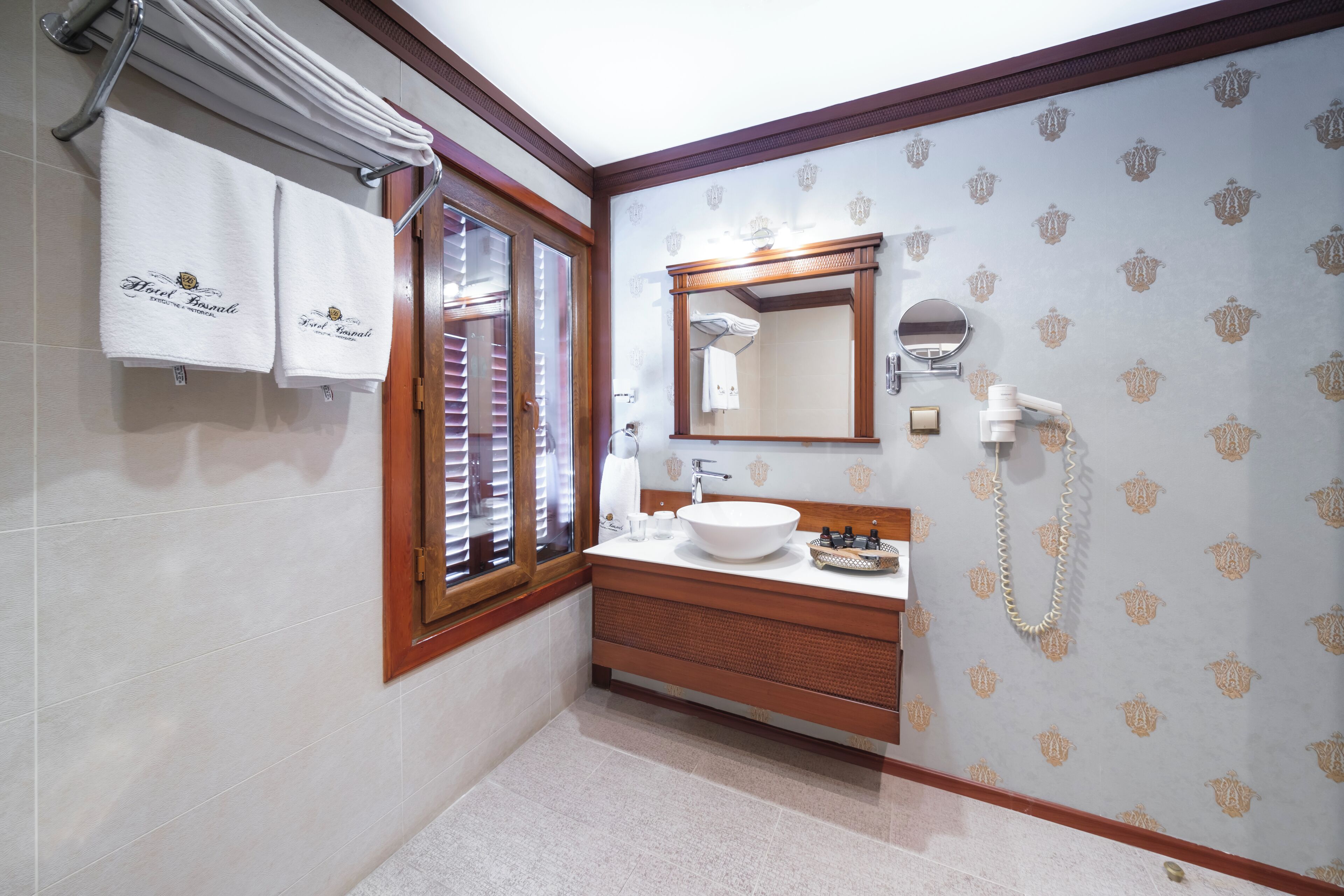 A bathroom with a wooden vanity, a round mirror, a sink, and a towel rack with two towels.