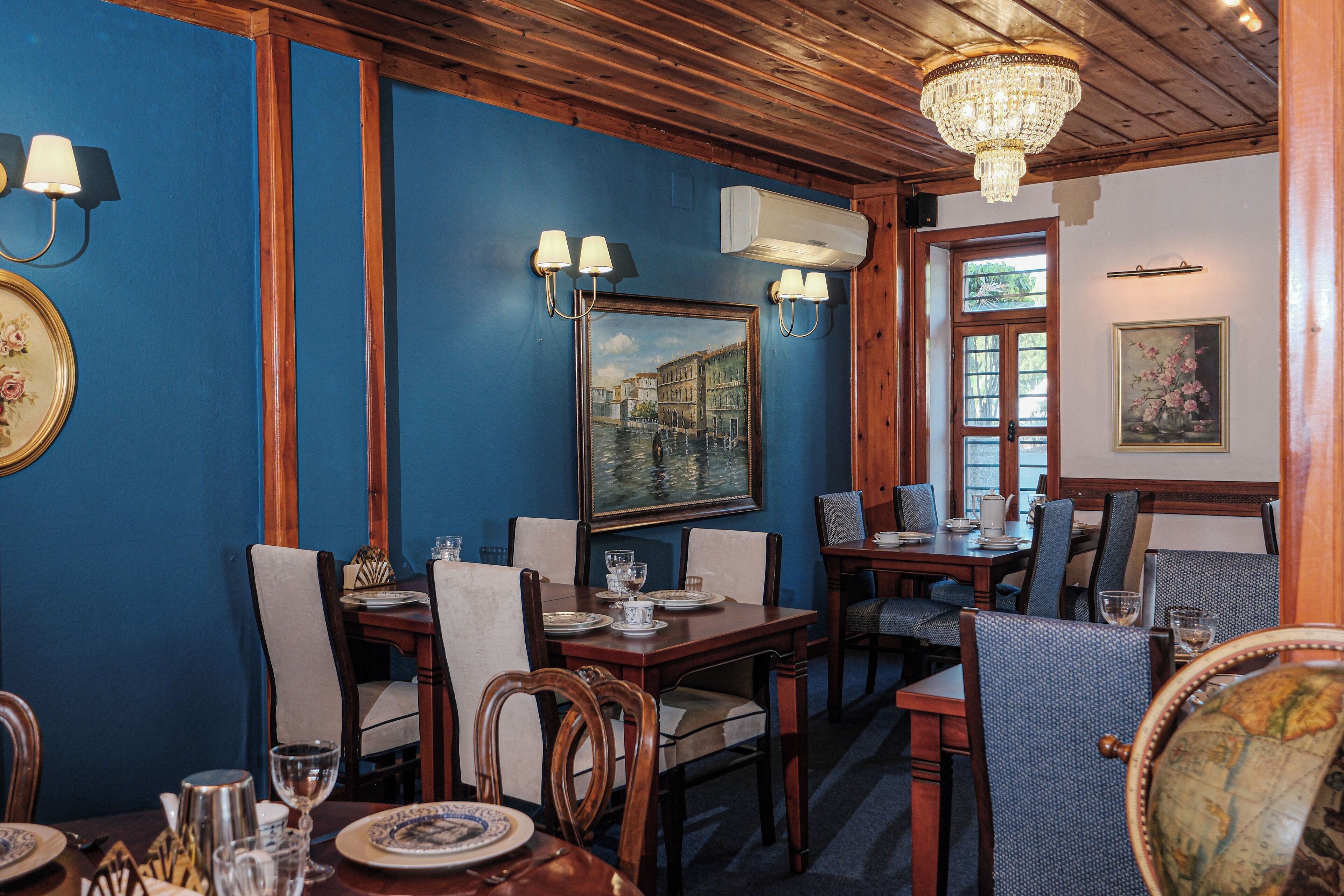 Un comedor con mesas y sillas de madera, una araña y lámparas de pared.