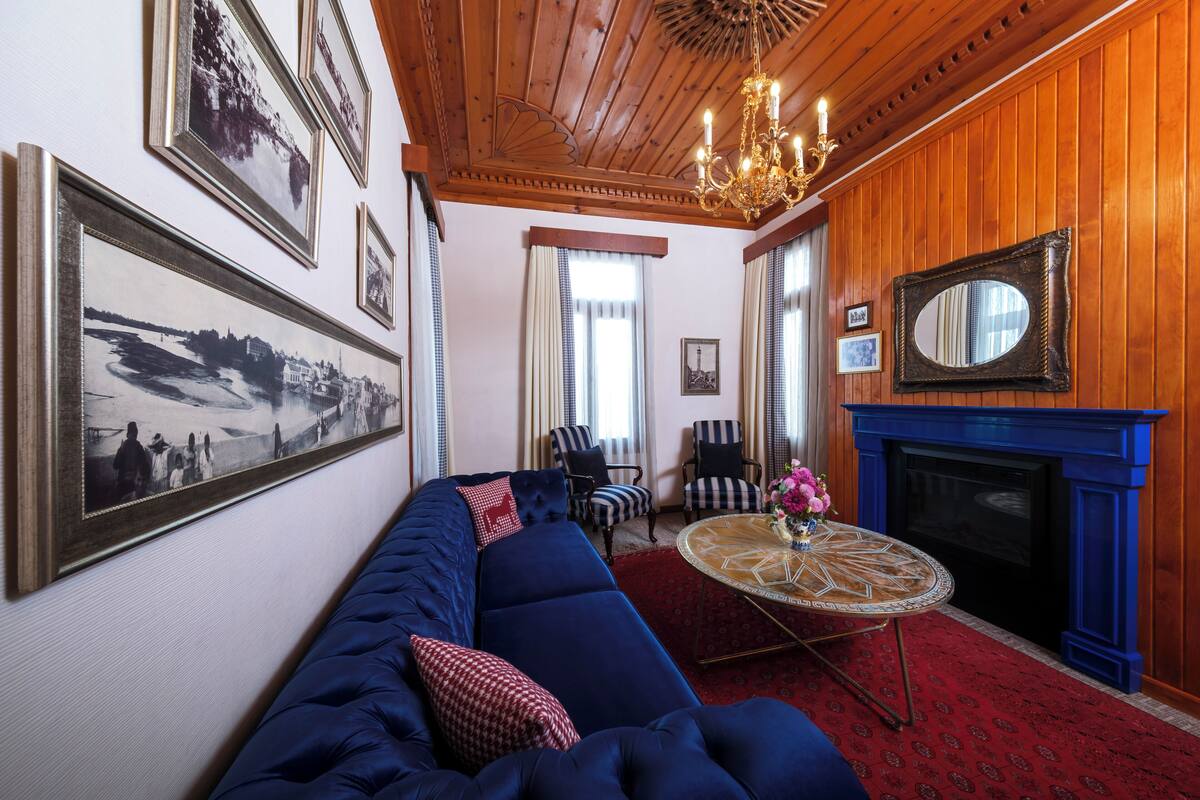 Une pièce avec un canapé bleu, une table ronde surmontée d’un vase, une cheminée et des tableaux encadrés accrochés au mur.