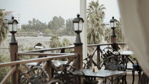 An outdoor seating area with tables and chairs, overlooking a body of water and palm trees. - Hotel Bosnali - Special Class (Adana)