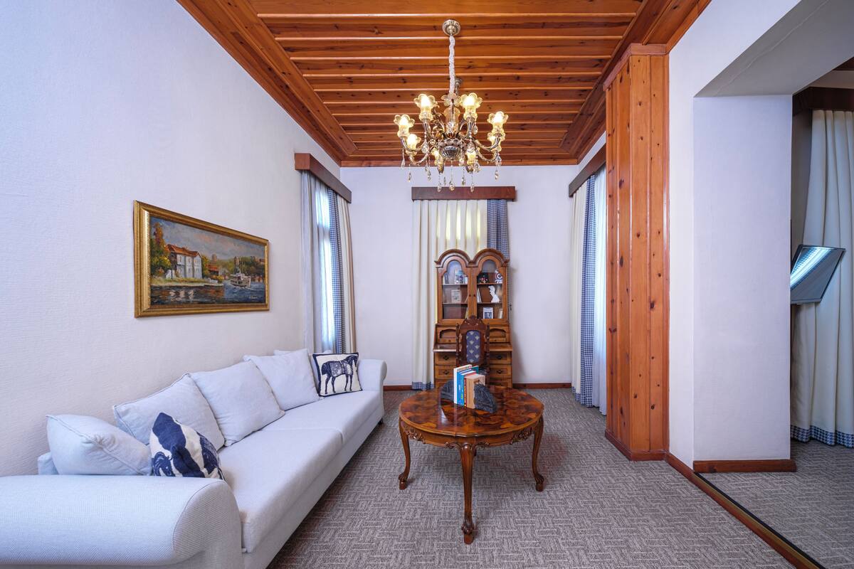 Un salon avec un plafond en bois, un lustre, un canapé agrémenté de coussins décoratifs, une table basse en bois et une bibliothèque.
