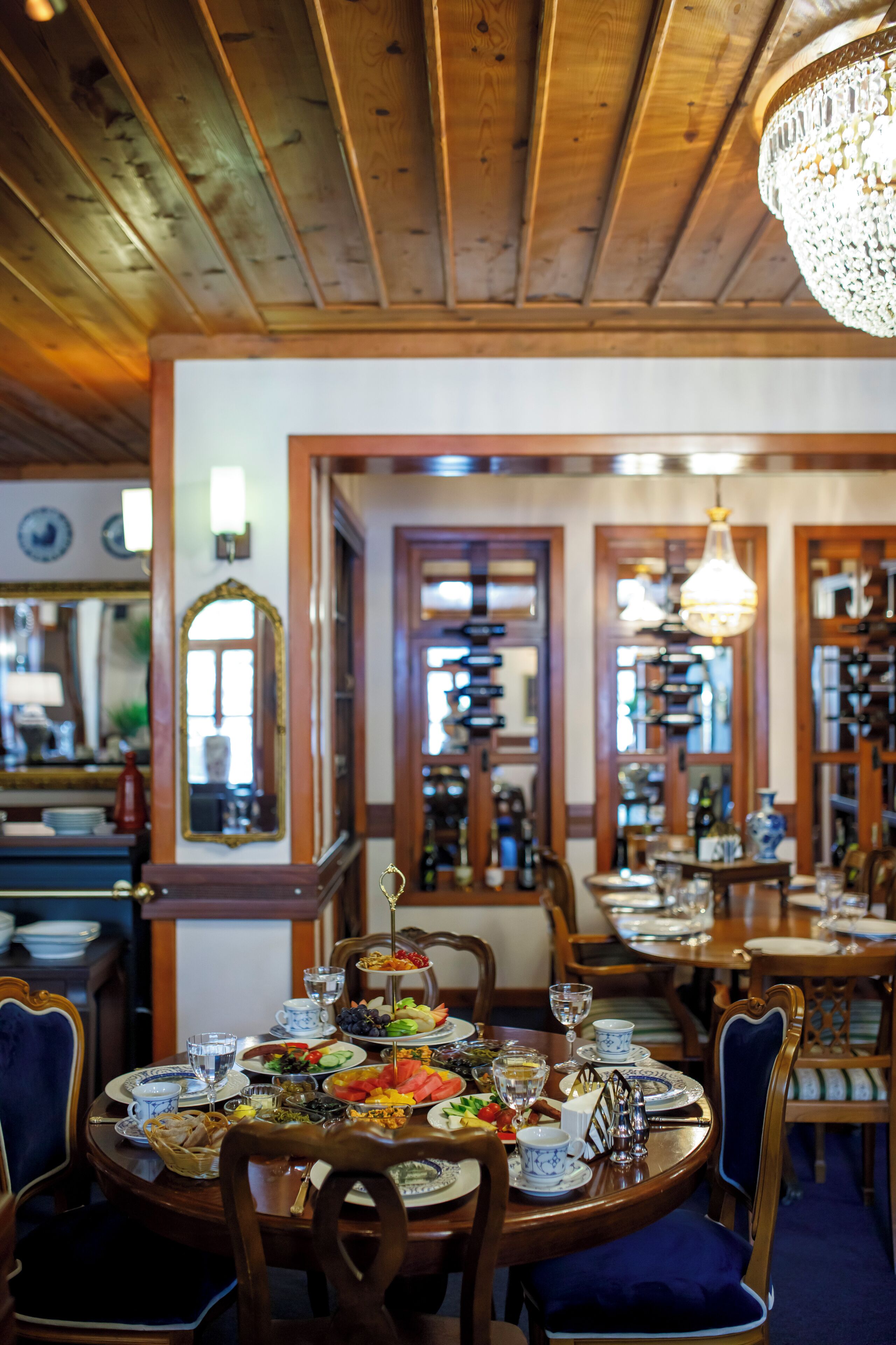 A dining area with wooden tables and chairs, a chandelier, and a mirror on the wall.