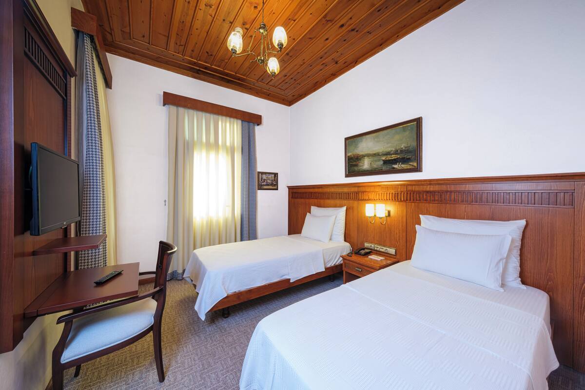 Une chambre d’hôtel avec deux lits, un bureau avec une chaise, une télévision et un tableau au mur.