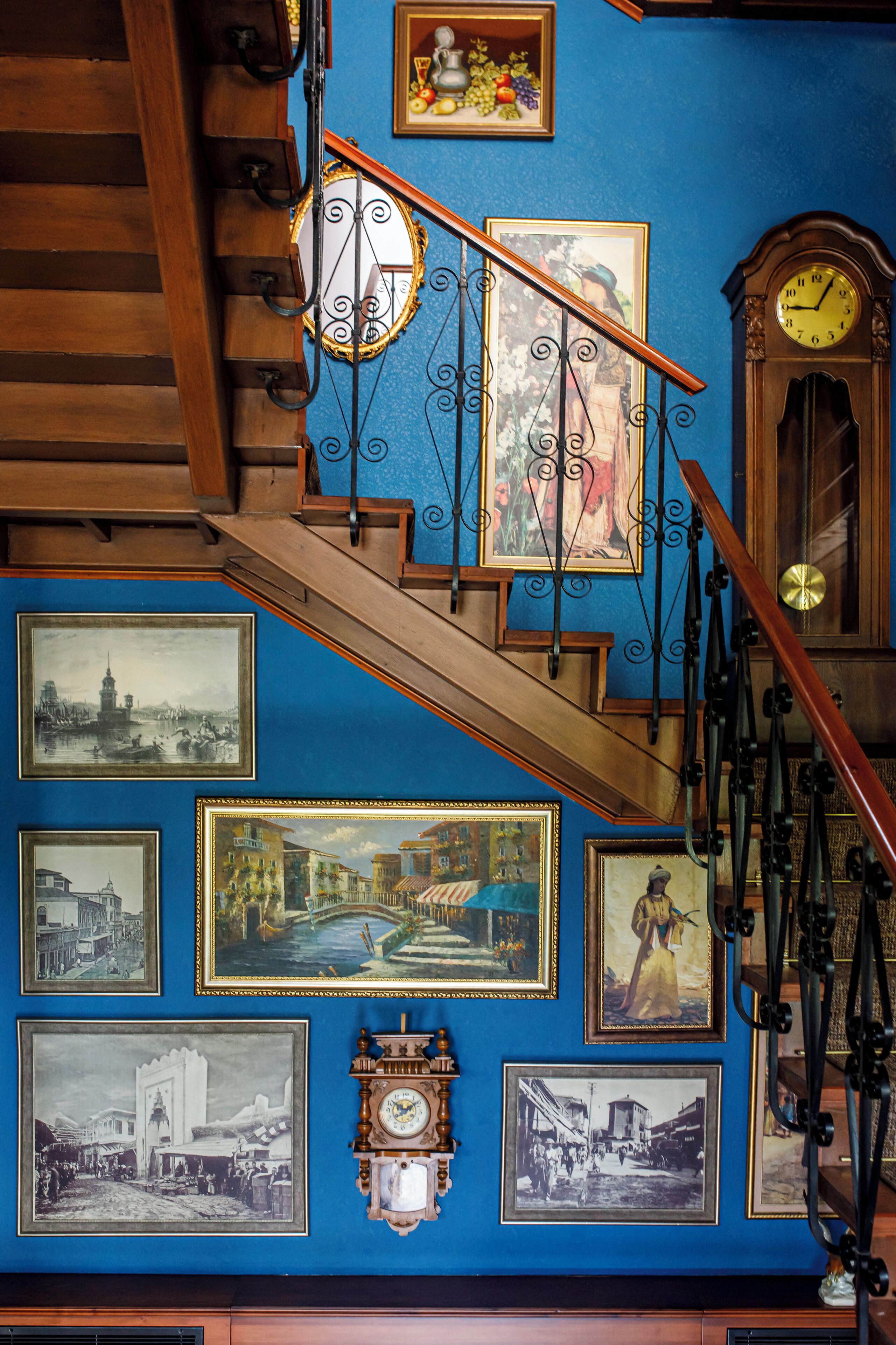 A staircase with ornate metal railings and a blue wall adorned with framed historical photographs and a clock.