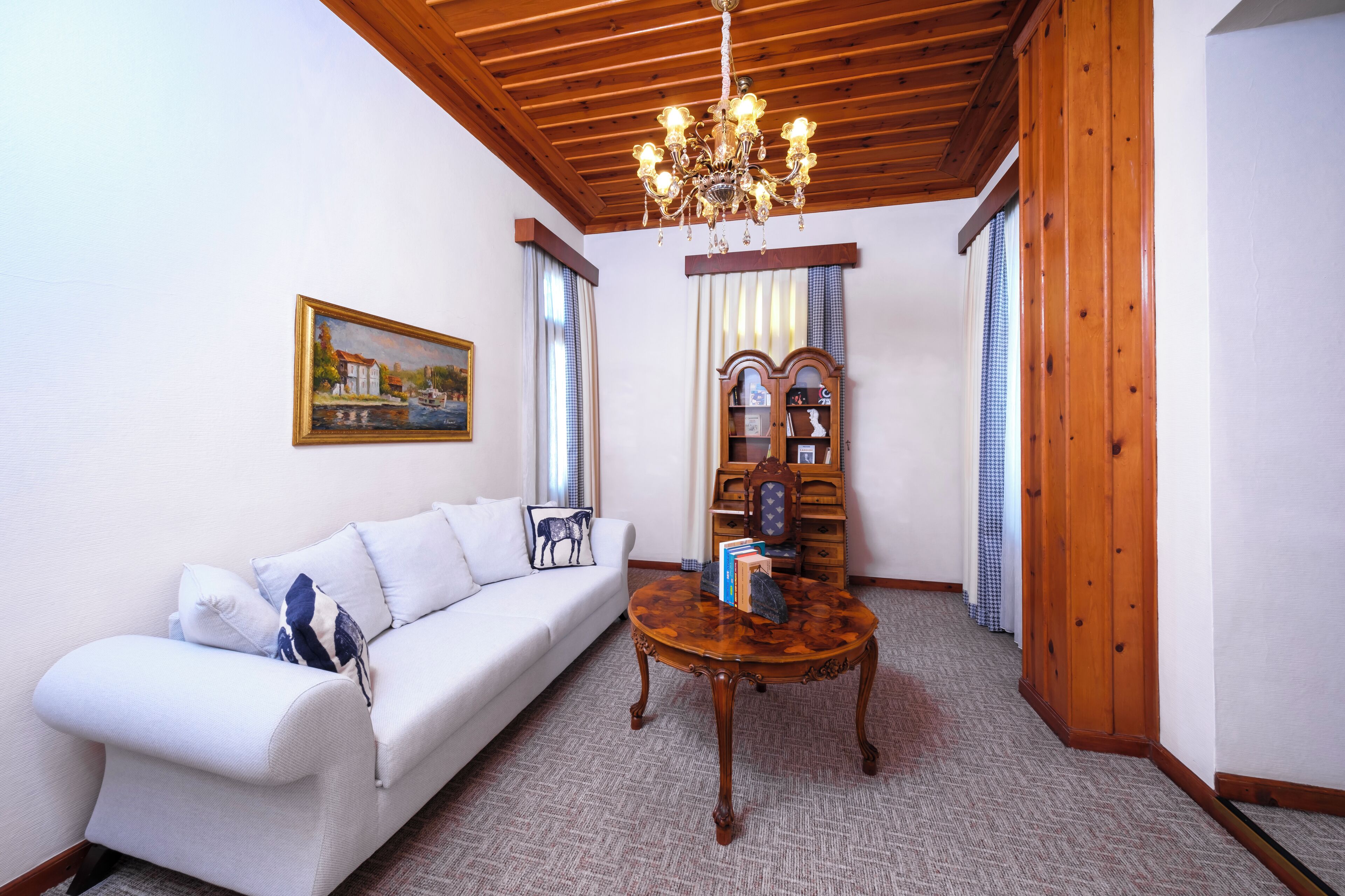 Una sala de estar con un sofá blanco, una mesa de centro de madera, una araña y un cuadro en la pared.