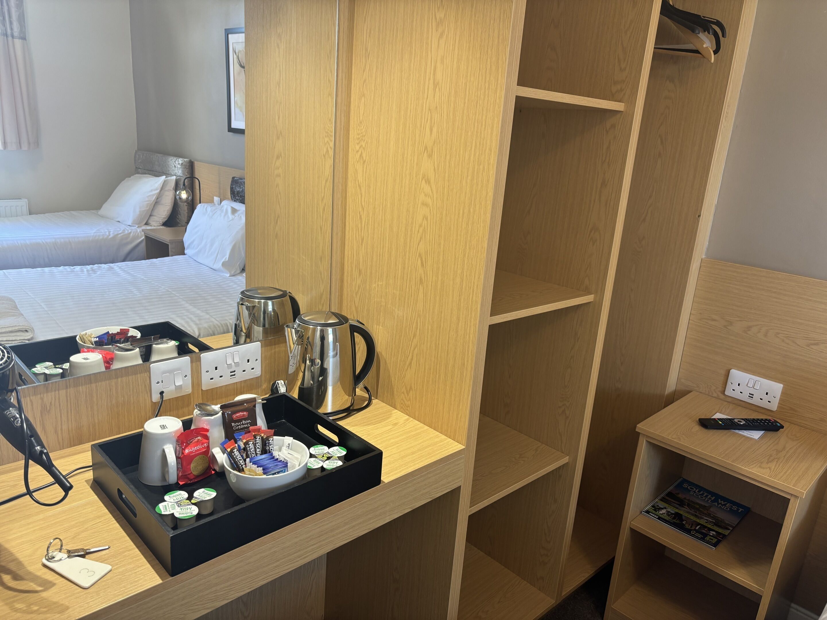 Habitación de hotel con un escritorio de madera, una bandeja con tazas de café, una tetera y una revista sobre una mesita.