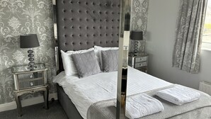 A bedroom with a tufted headboard, a bed with white linens, two bedside tables with lamps, and a window with curtains. - Solway Lodge Hotel (Gretna)
