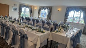 A conference room with long tables, chairs with blue sashes, and floral centerpieces. - Solway Lodge Hotel (Gretna)