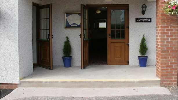 A building entrance with a reception sign, two potted plants, and a framed picture on the wall. - Solway Lodge Hotel (Gretna)