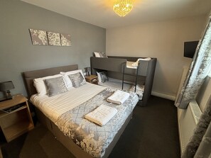 Une chambre bien rangée, avec un grand lit, une table de chevet, un petit bureau et une chaise.