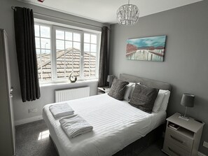 Un lit bien fait, avec des oreillers et des serviettes pliées, une table de chevet avec une lampe, un tableau au mur et une fenêtre avec des rideaux.