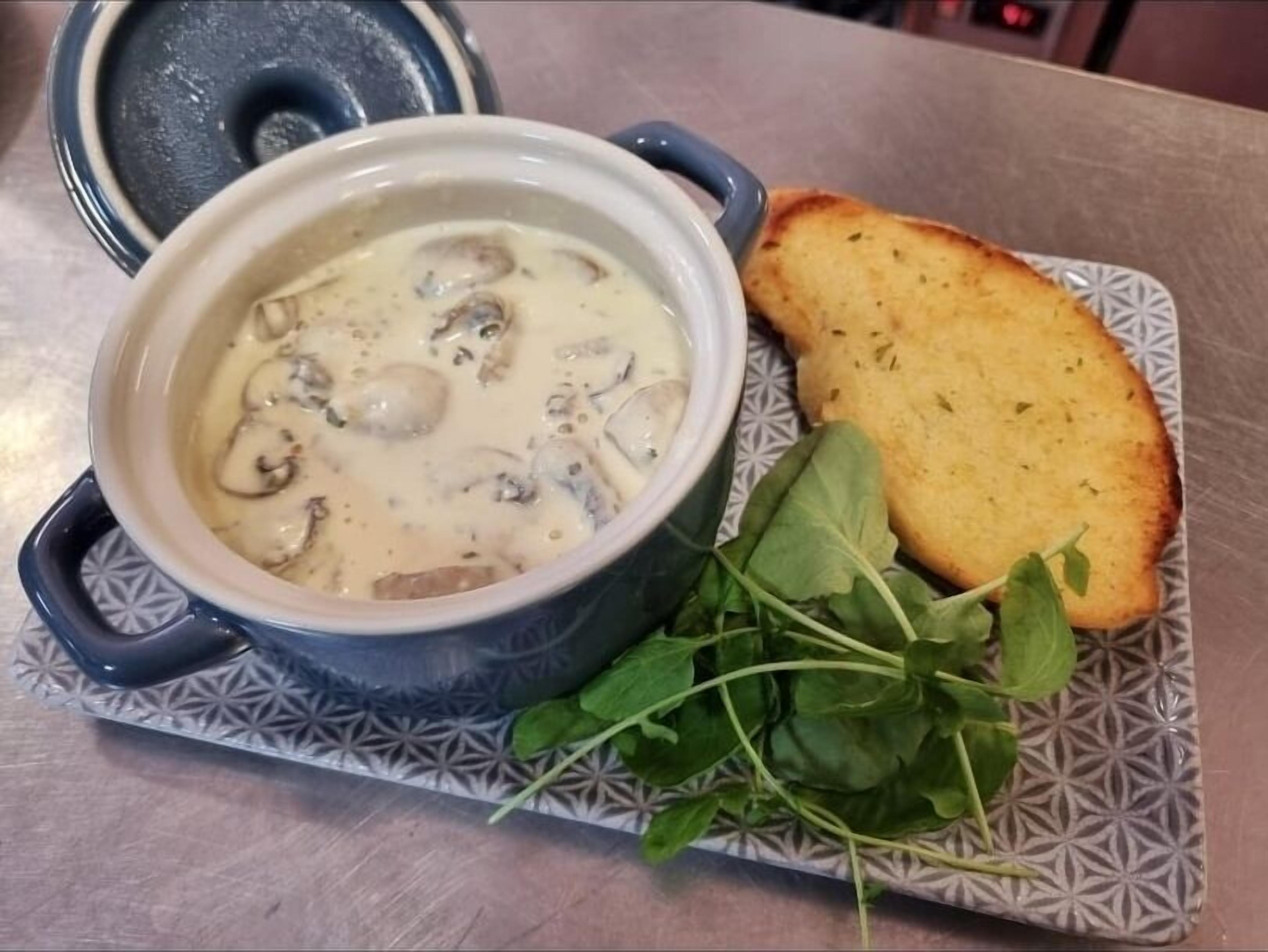 A bowl of creamy soup with mushrooms, accompanied by a slice of toasted bread and fresh greens on a patterned plate.