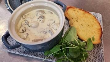 A bowl of creamy soup with mushrooms, accompanied by a slice of toasted bread and fresh greens on a patterned plate.