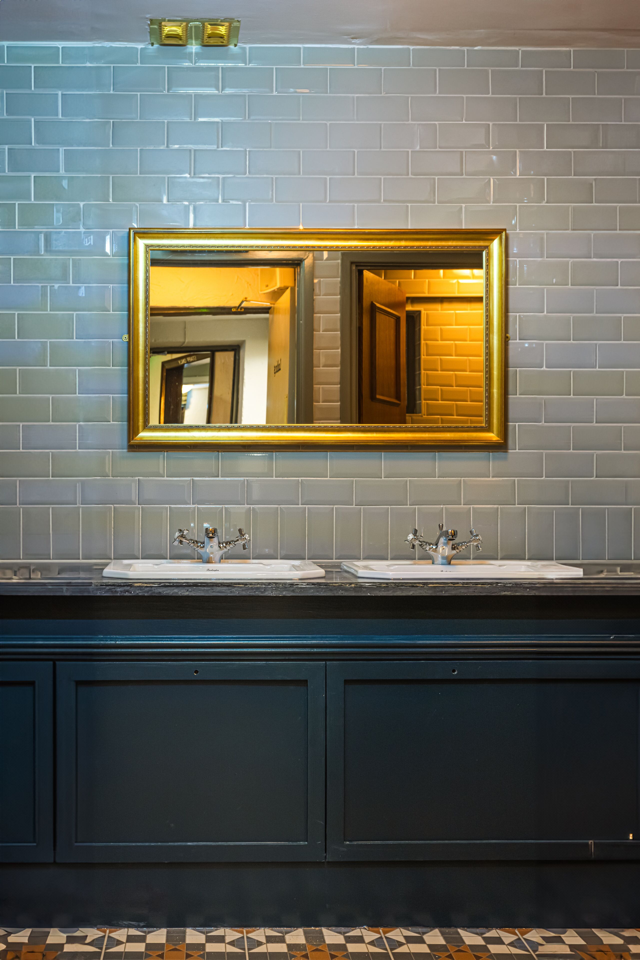 A bathroom with a large mirror, two sinks, and a tiled wall.