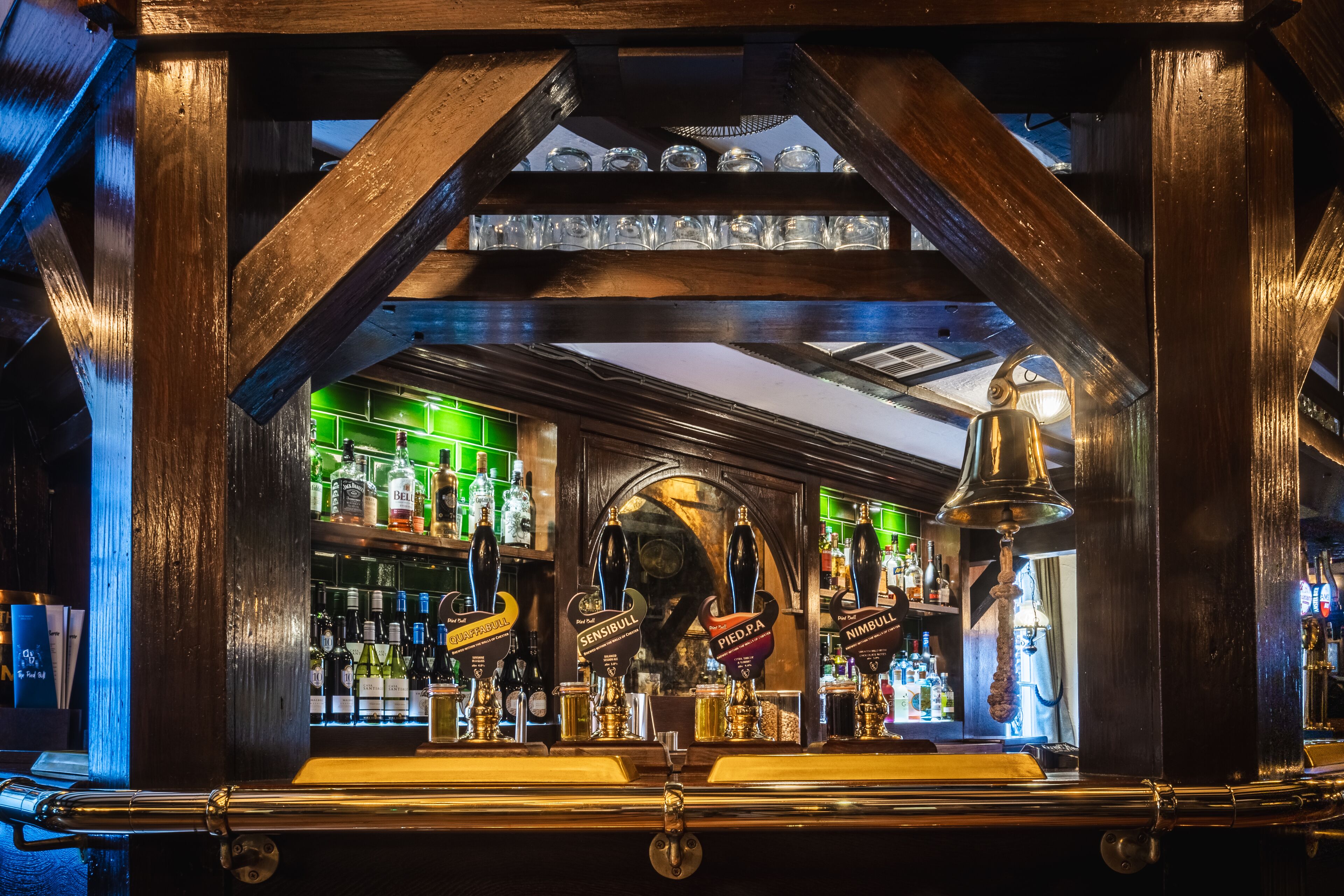 Zona de bar con vigas de madera, mostrador iluminado en verde y diversas botellas de licor.