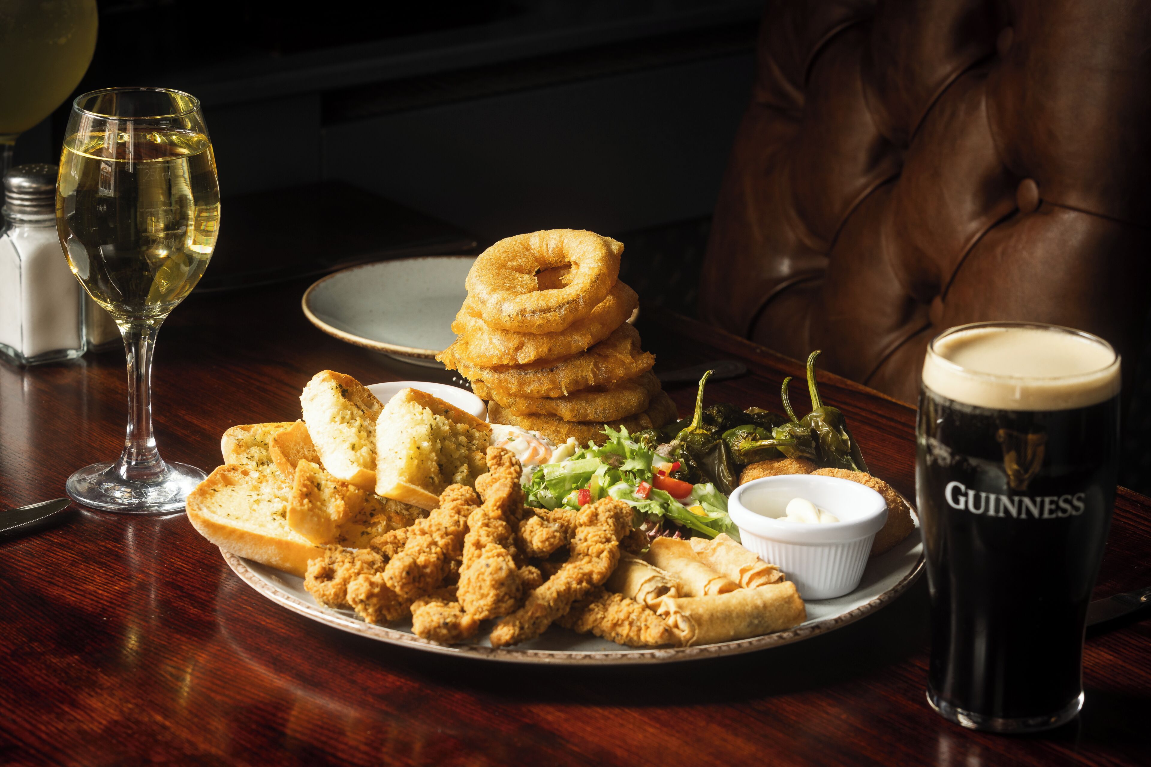 A plate of fried chicken, onion rings, and vegetables with a glass of wine and a glass of Guinness beer on a wooden table.