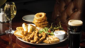 A plate of fried chicken, onion rings, and vegetables with a glass of wine and a glass of Guinness beer on a wooden table.