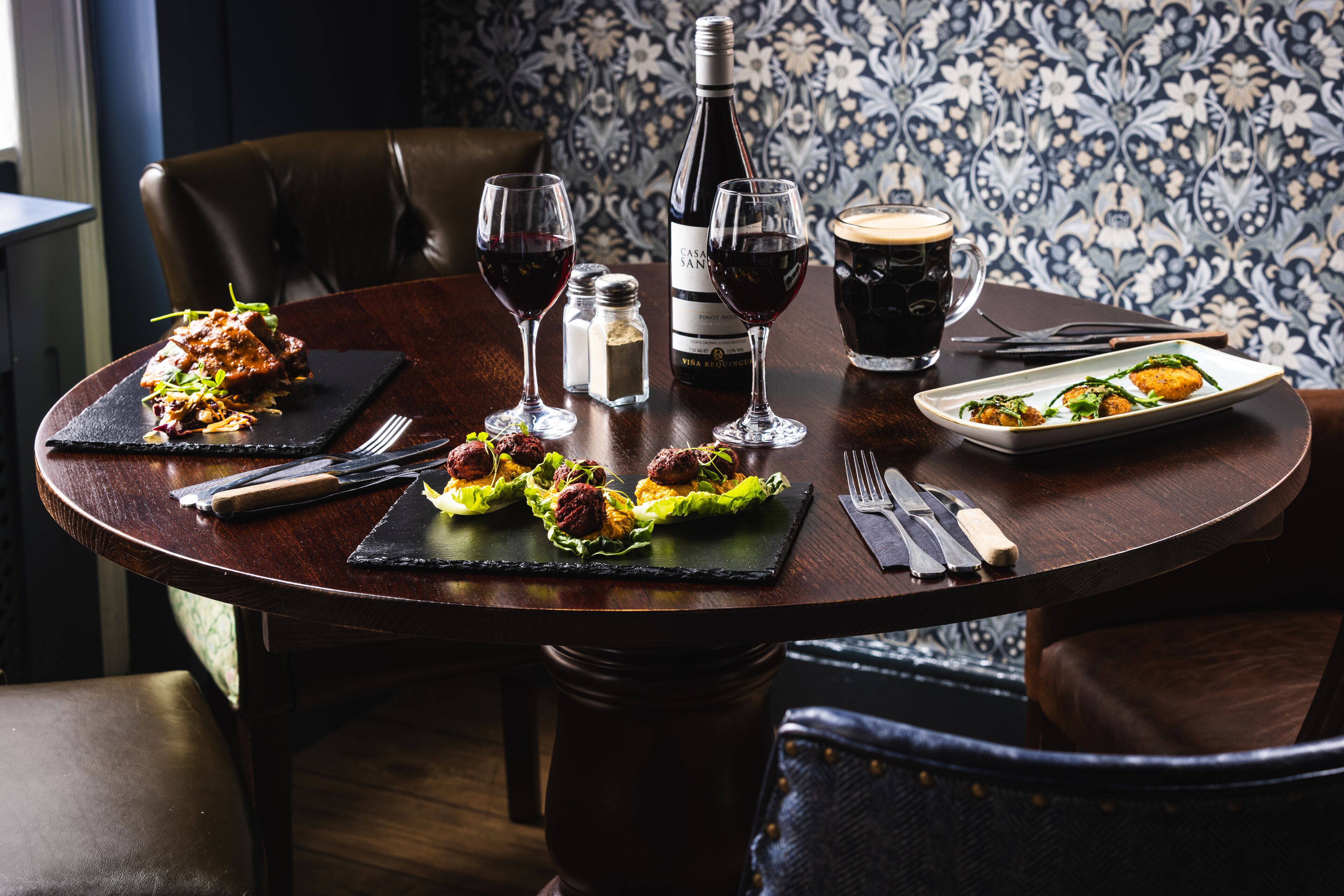 A dining table set with plates of food, wine glasses, a bottle of wine, and a coffee mug.
