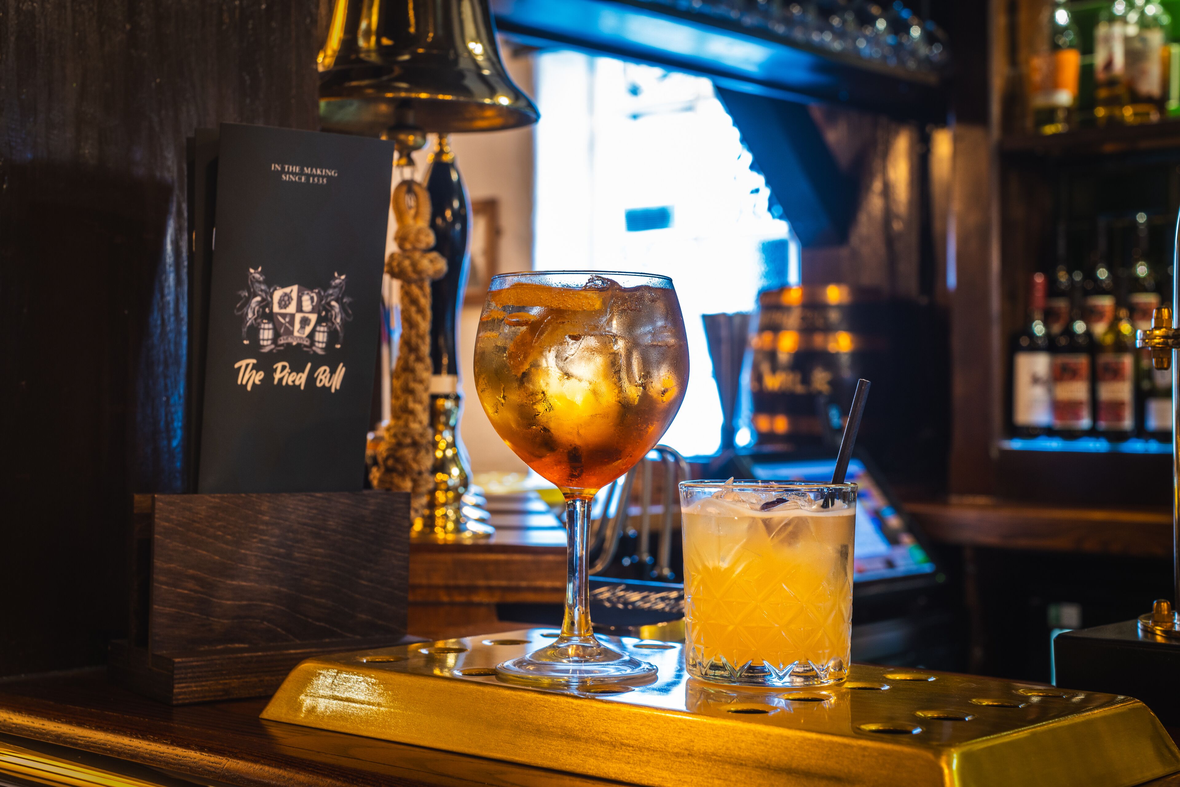 A bar setting with a glass of amber-colored drink, a cocktail glass, and a menu stand.