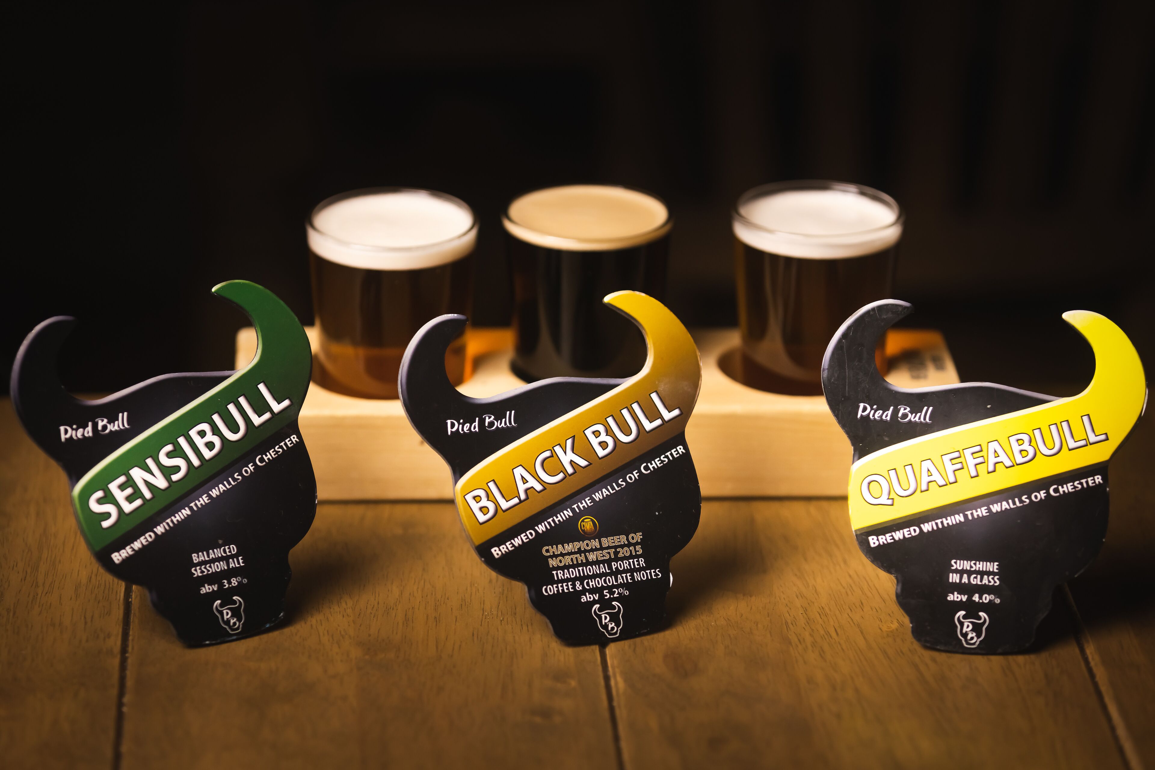 Three beer bottles with labels on a wooden surface.