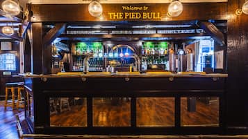 A bar with a wooden counter, multiple beer taps, and a sign reading "Welcome to THE PIED BULL".