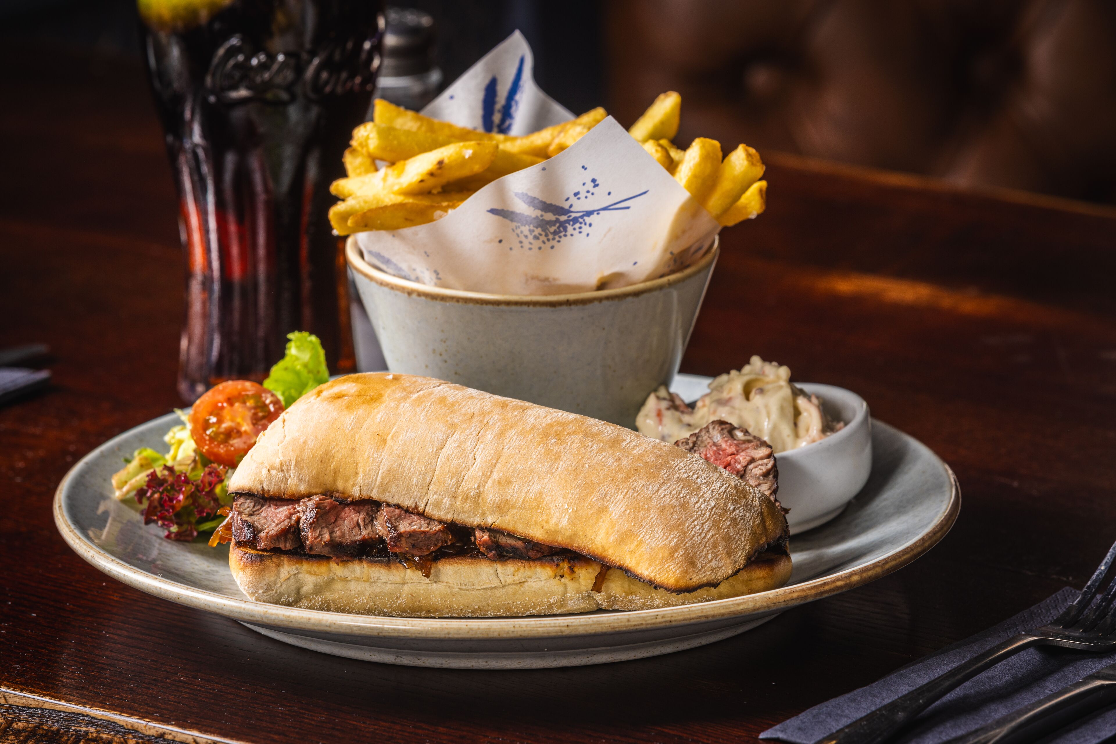 A plate with a sandwich, fries, and a small bowl of sauce.