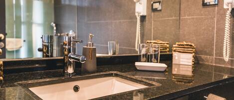 A modern bathroom with a black granite countertop, a white sink, a mirror, and a hairdryer mounted on the wall.