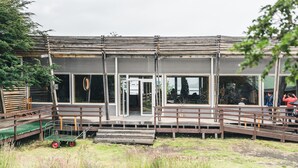 A modern building with large windows and a wooden deck. - Hotel Lago Grey (Torres del Paine)