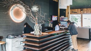 A modern reception desk with a wooden counter, a glass vase with branches, and a wall-mounted circular light fixture. - Hotel Lago Grey (Torres del Paine)