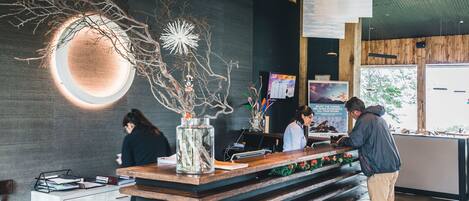 A modern reception desk with a wooden counter, a glass vase with branches, and a wall-mounted circular light fixture.