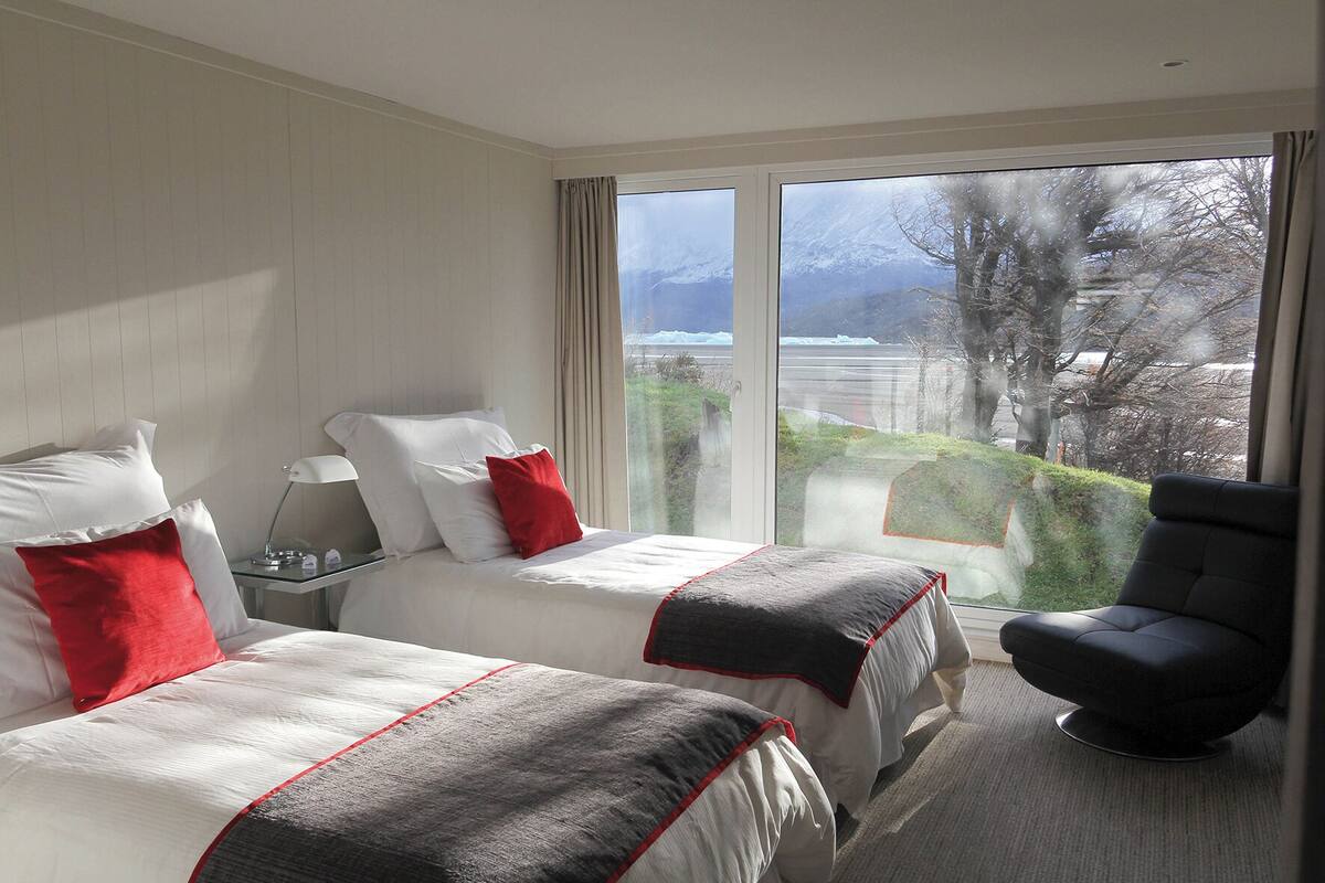 Ein Hotelzimmer mit zwei Betten, einem Sessel und einem großen Fenster mit Blick auf eine verschneite Landschaft.