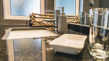 A modern bathroom with a granite countertop, a square sink, a soap dispenser, and a glass of water.