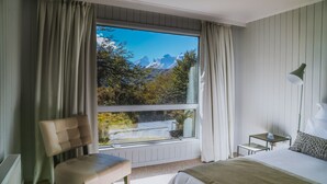 A bedroom with a large window, a bed, a chair, a table, and a lamp. - Hotel Lago Grey (Torres del Paine)