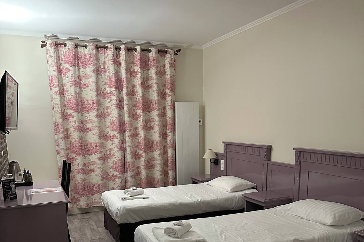 A hotel room with two beds, a desk, a chair, a lamp, and a mirror.