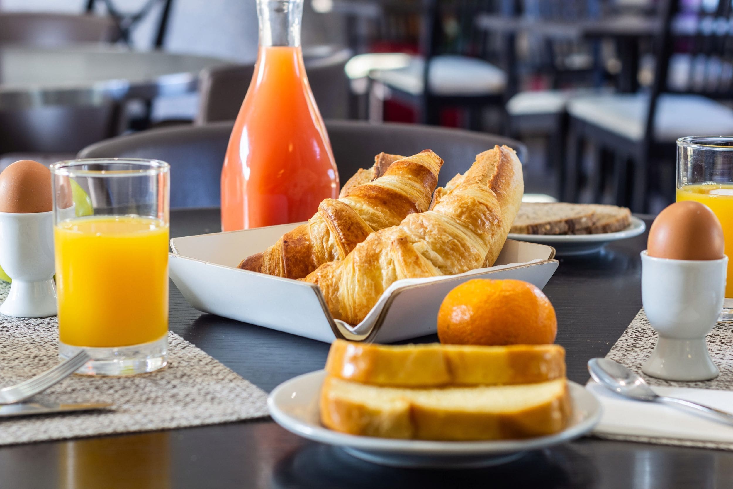 A breakfast setting with croissants, orange juice, and a bottle of orange juice on a table.