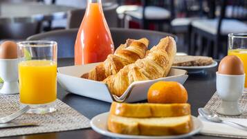 A breakfast setting with croissants, orange juice, and a bottle of orange juice on a table.