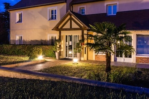 A two-story house with a well-lit entrance, a small porch, and a garden with a palm tree.