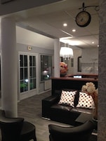 A modern living room with a black leather sofa, a chandelier, and a clock on the wall.