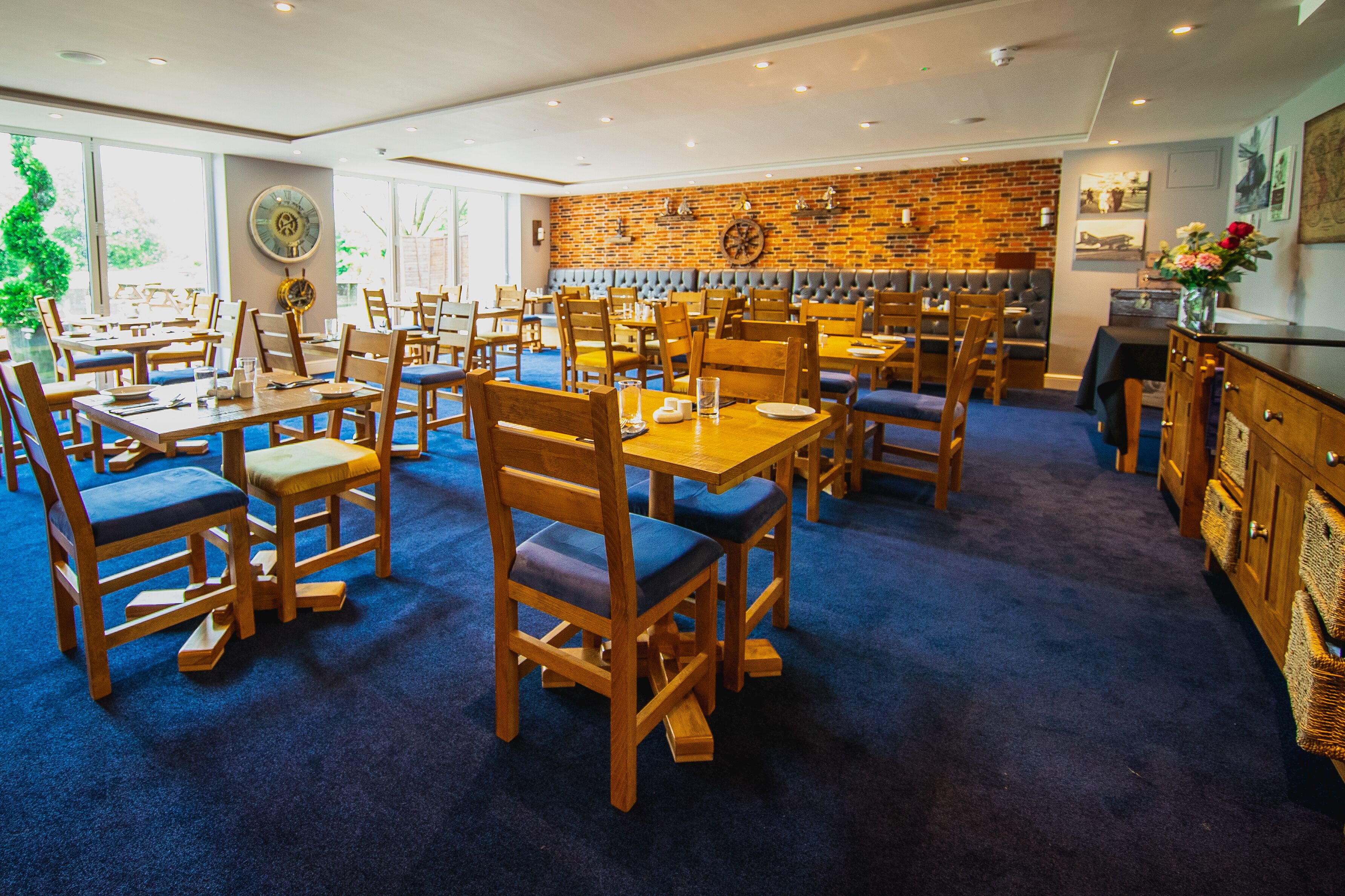 Un restaurant avec des tables et des chaises en bois, un mur en briques et une moquette bleue.