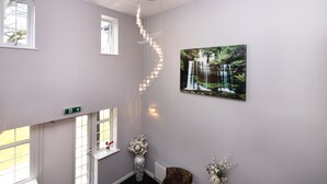 Um interior moderno com escada, iluminação pendente, fotografia emoldurada da natureza e um vaso com flores.
