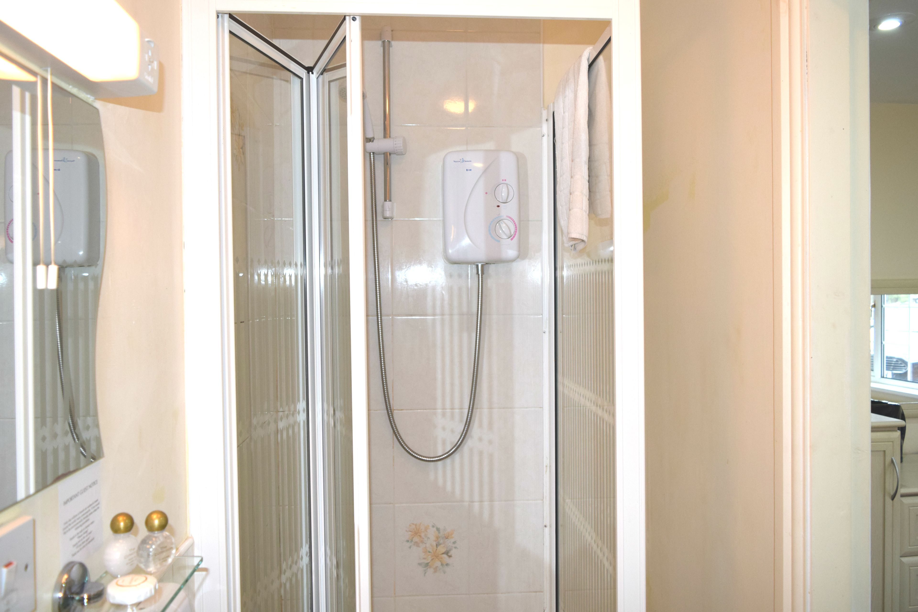 A shower with a handheld showerhead and a wall-mounted control panel.