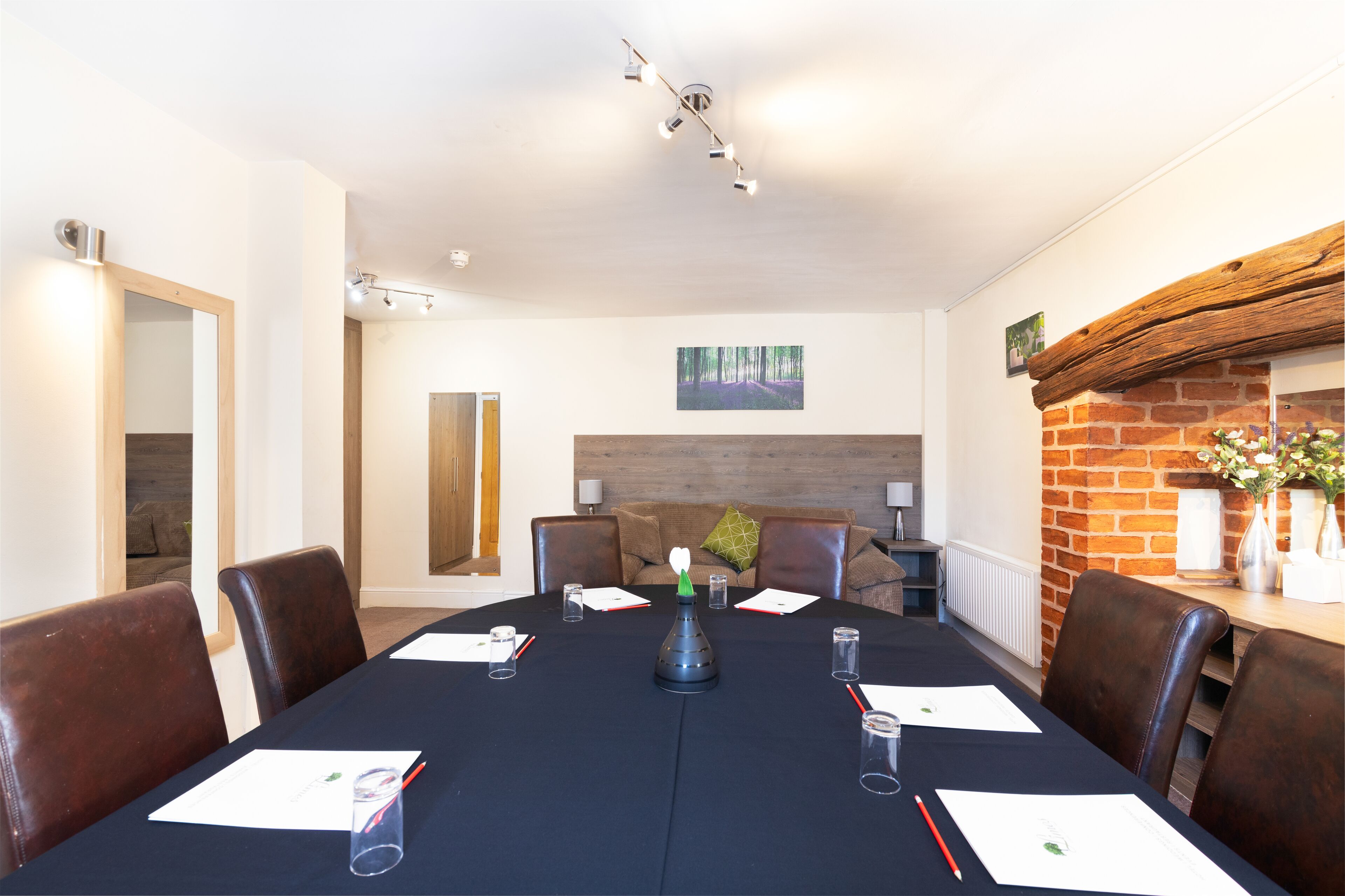A conference room with a long table, brown leather chairs, a black tablecloth, and a vase with flowers on the right side.