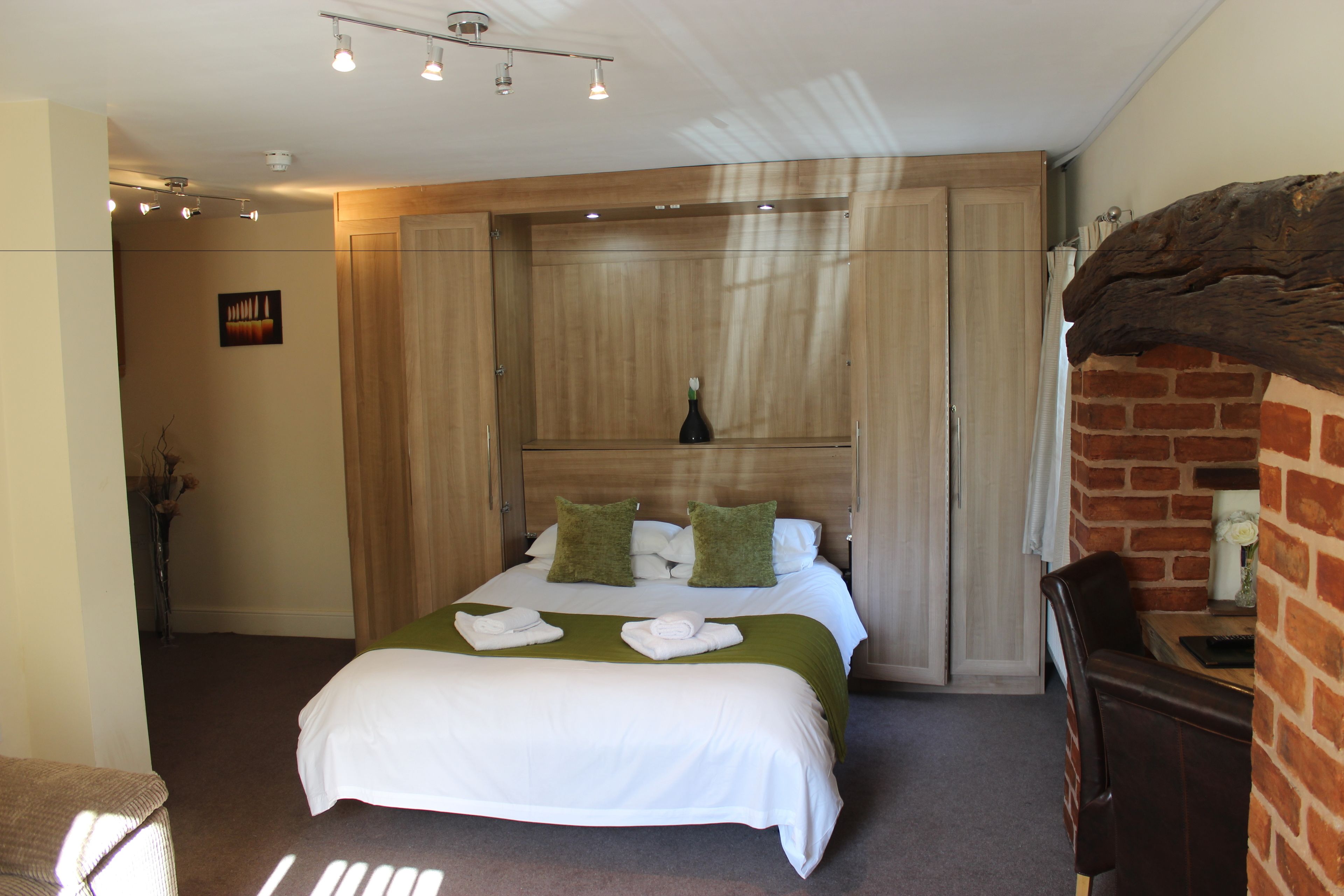 Een hotelkamer met een bed, een houten garderobe, een bakstenen muur en een kleine tafel met een vaas.
