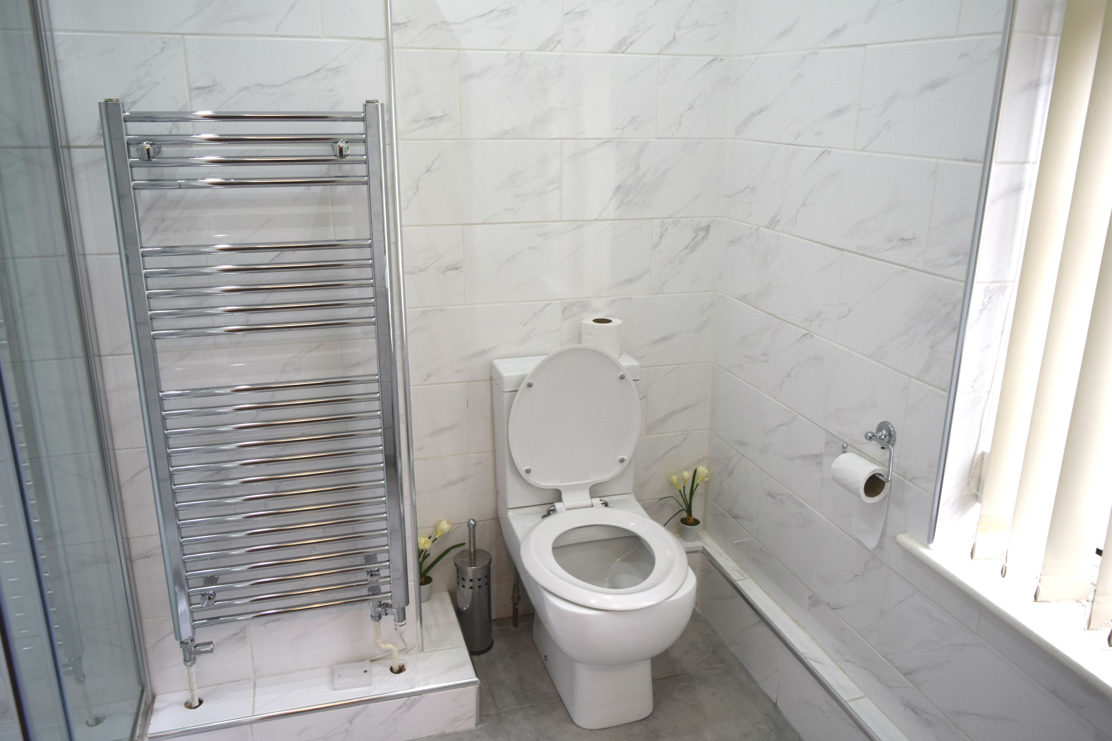 Een badkamer met een wit toilet, een douchecabine van glas en een wand betegeld met marmer.